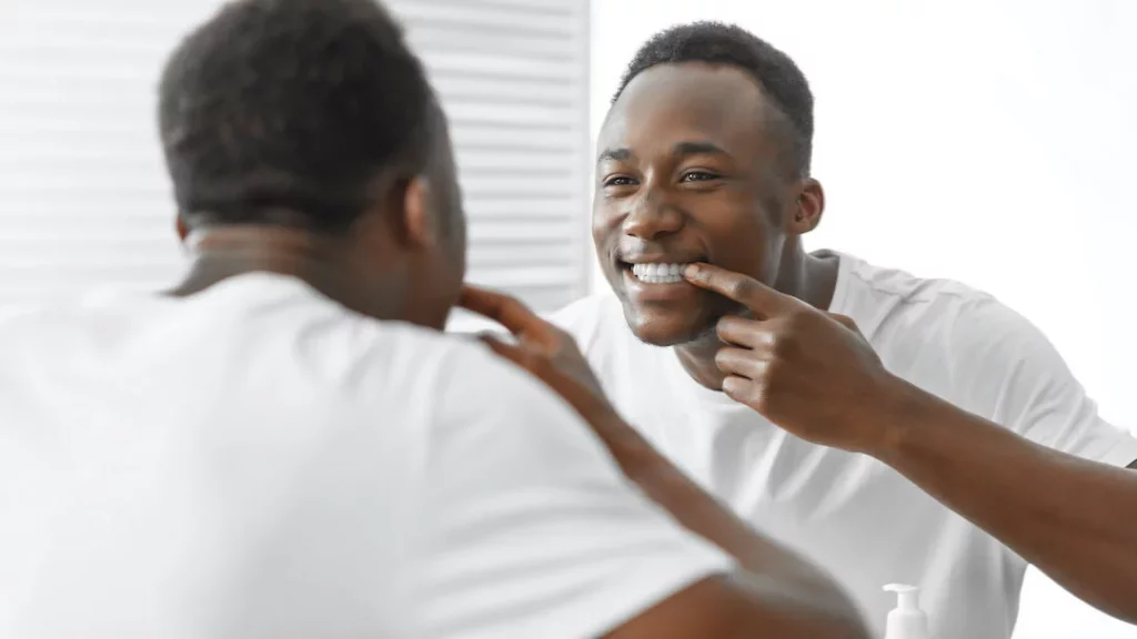 Tooth Pain After Whitening - African Man Smiling to Mirror Post Teeth Whitening Procedure